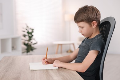 Photo of Boy with correct posture doing homework at wooden desk indoors