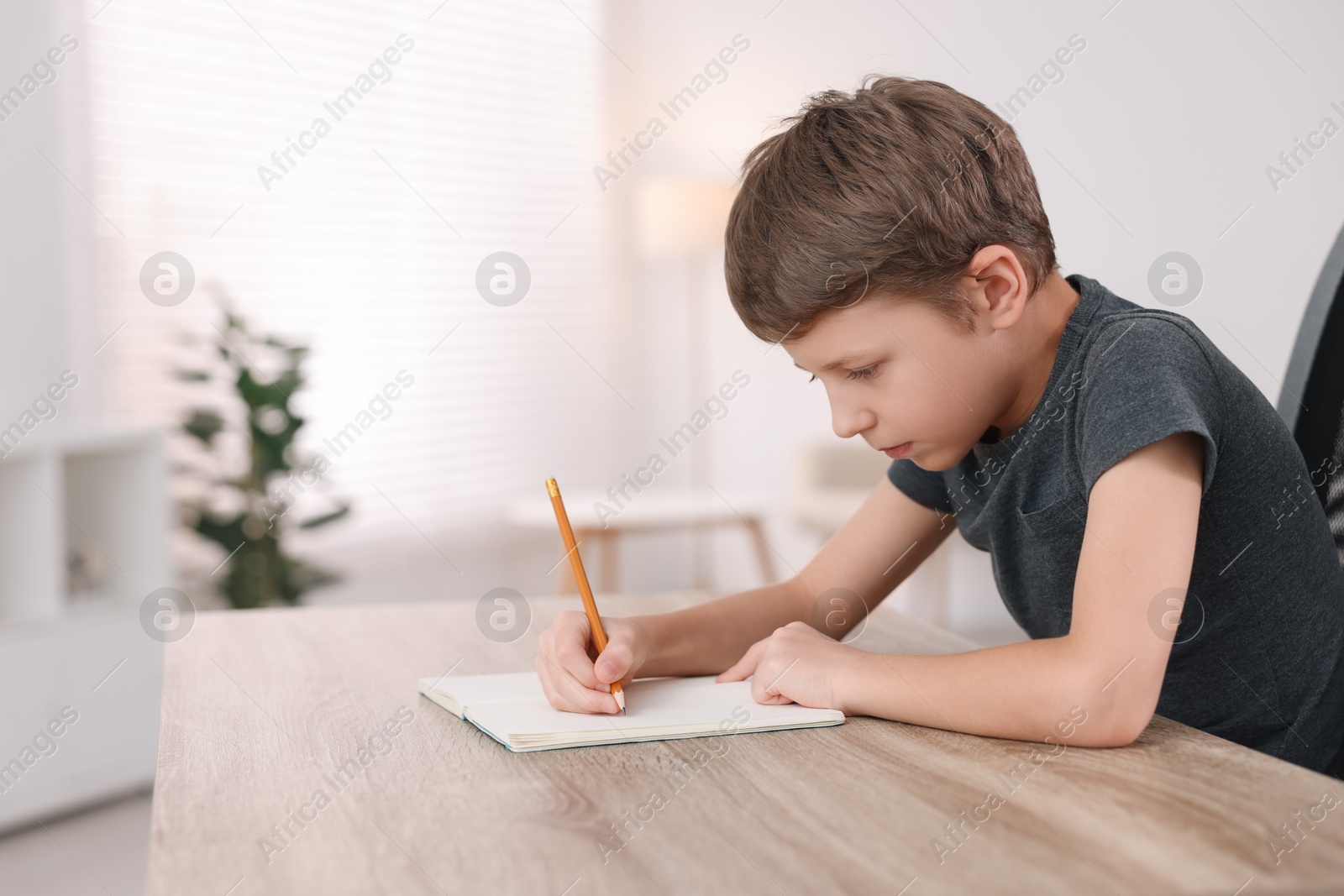 Photo of Boy with incorrect posture using laptop at wooden desk indoors