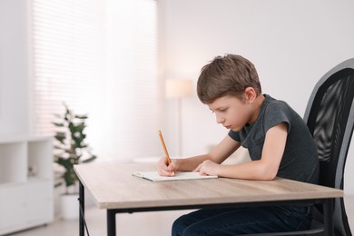 Photo of Boy with incorrect posture using laptop at wooden desk indoors