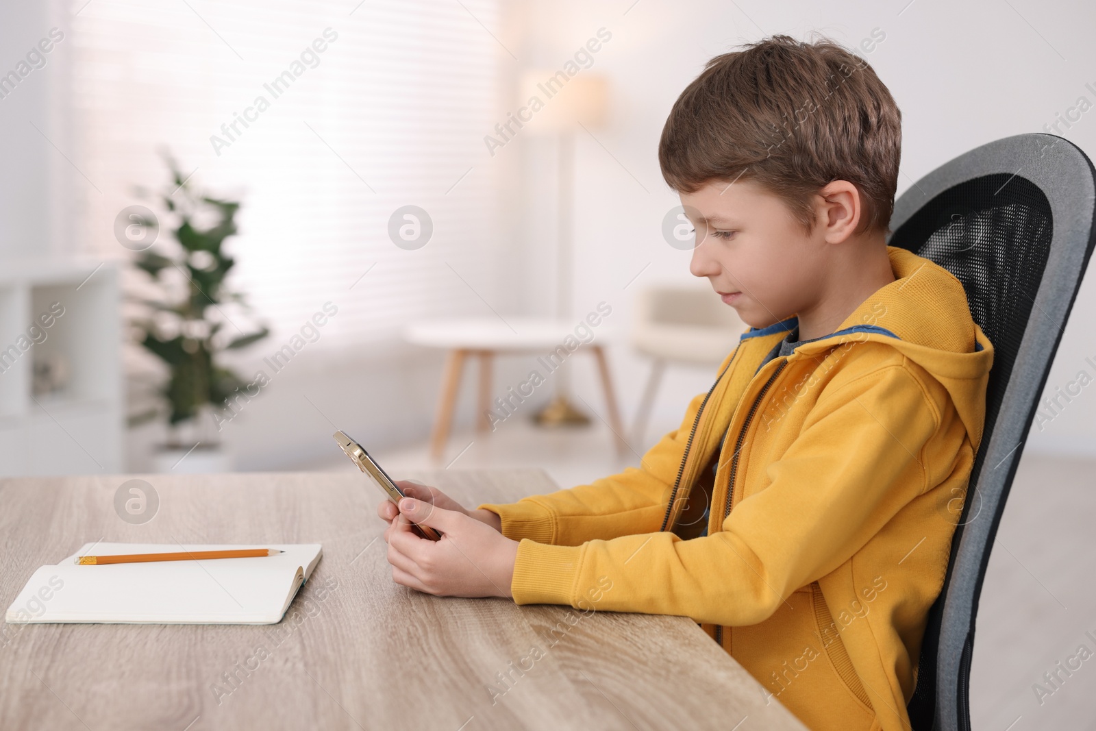 Photo of Boy with correct posture using smartphone at wooden desk indoors