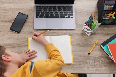 Photo of Boy with incorrect posture doing homework at wooden desk indoors, top view