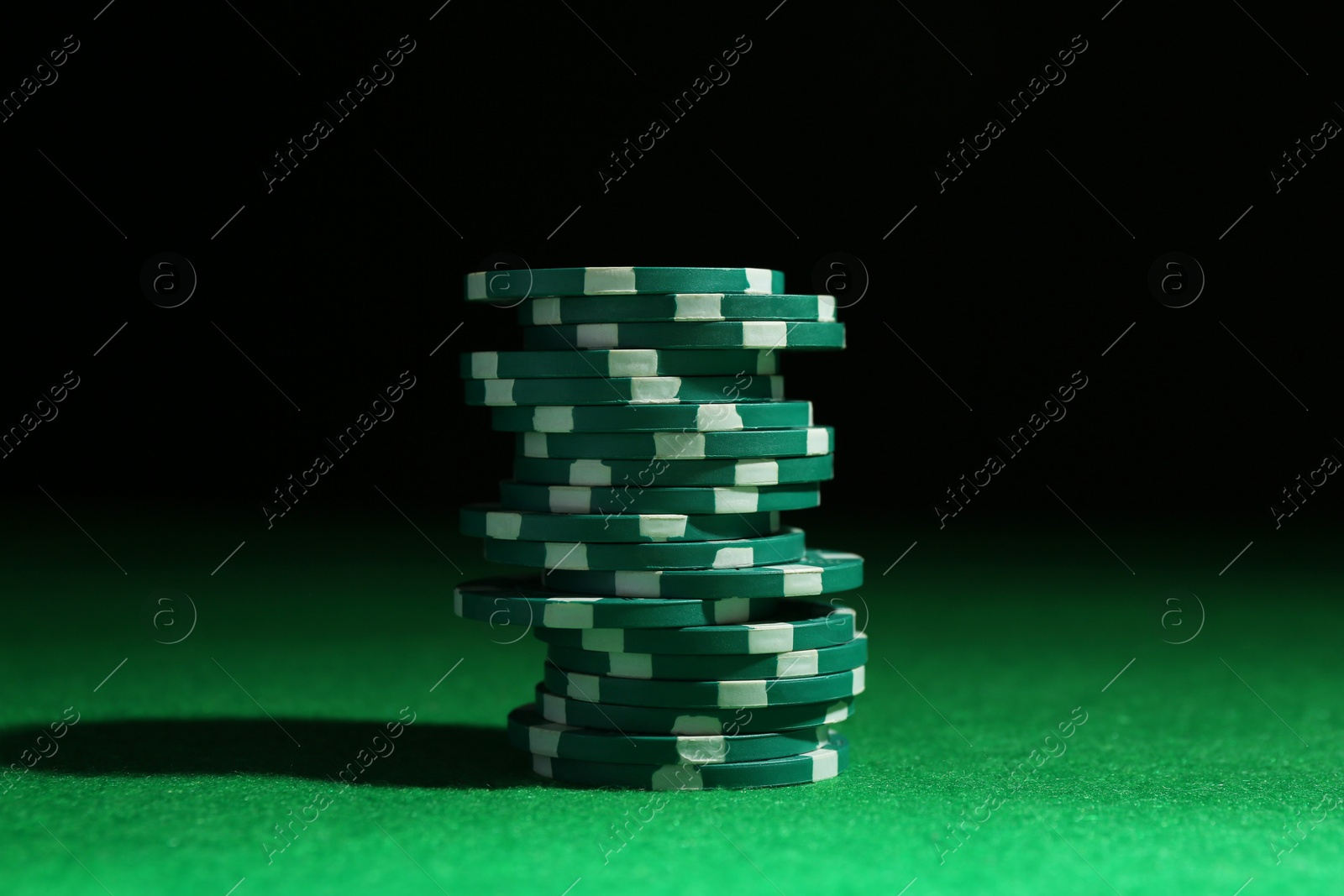 Photo of Stack of poker chips on green table against dark background, closeup