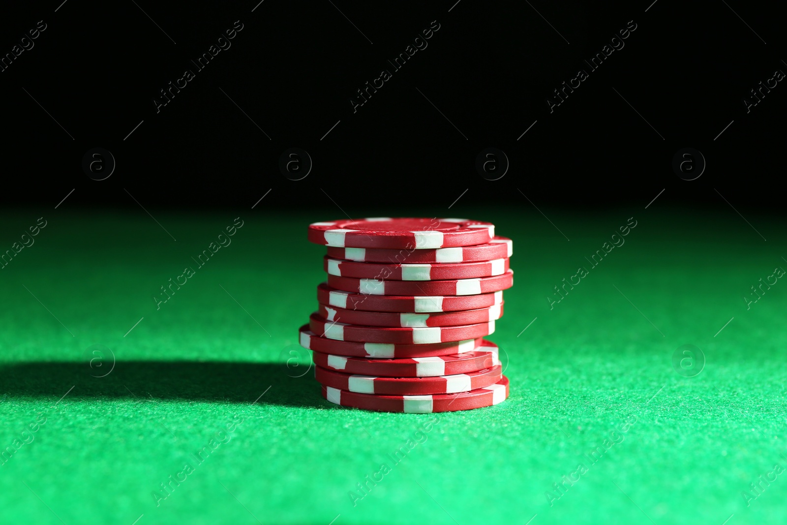 Photo of Stack of poker chips on green table against dark background, closeup