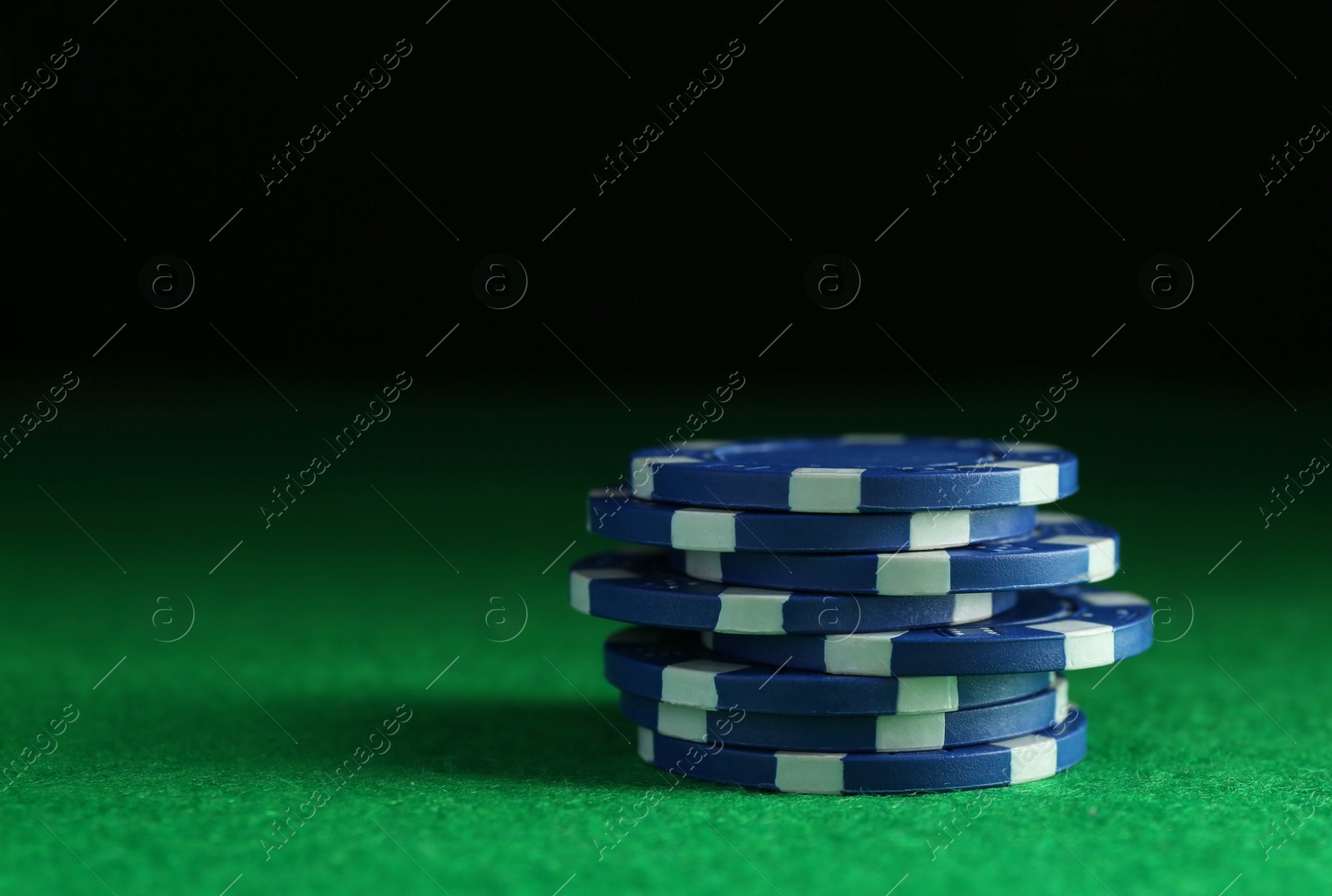 Photo of Stack of poker chips on green table against dark background, closeup. Space for text