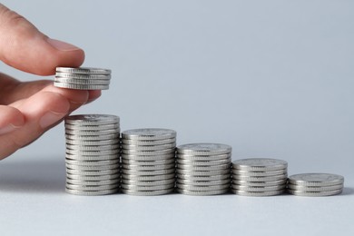 Photo of Salary concept. Woman putting coins on stack against light grey background, closeup