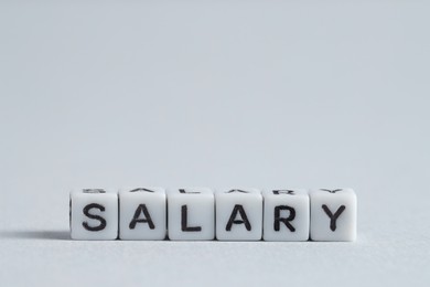 Photo of Word Salary made of cubes on light grey background, space for text