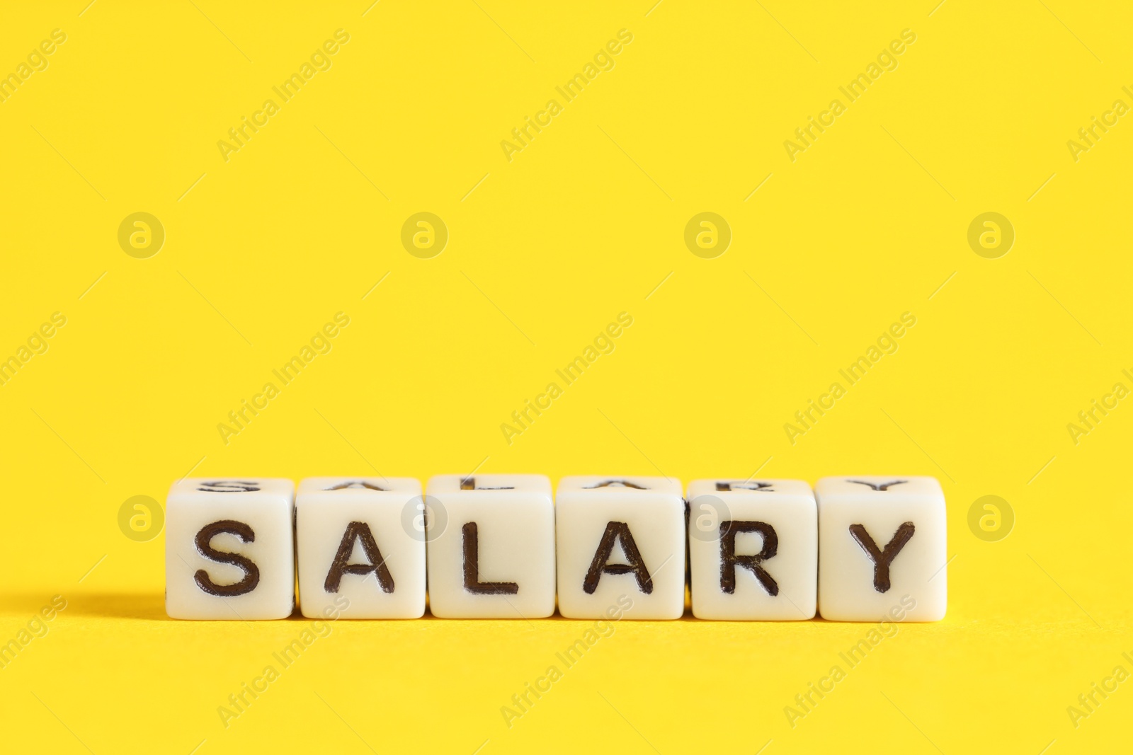 Photo of Word Salary made of cubes on yellow background, space for text