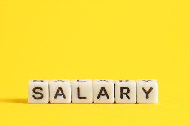 Photo of Word Salary made of cubes on yellow background, space for text