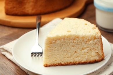 Photo of Piece of delicious sponge cake and fork on wooden table, closeup