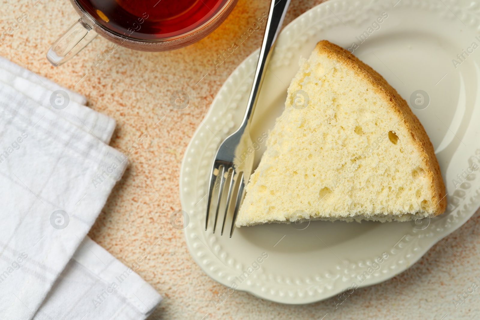 Photo of Piece of delicious sponge cake served on beige textured table, flat lay