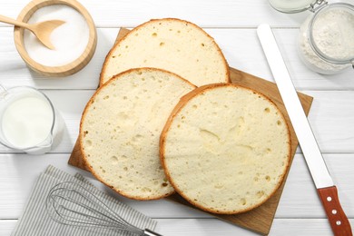 Photo of Delicious cut sponge cake, ingredients and knife on white wooden table, flat lay