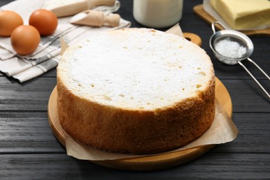 Photo of Delicious sponge cake and ingredients on black wooden table