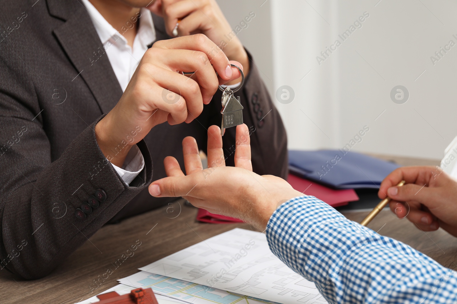 Photo of Real estate agent giving house key to new owner at wooden table, closeup