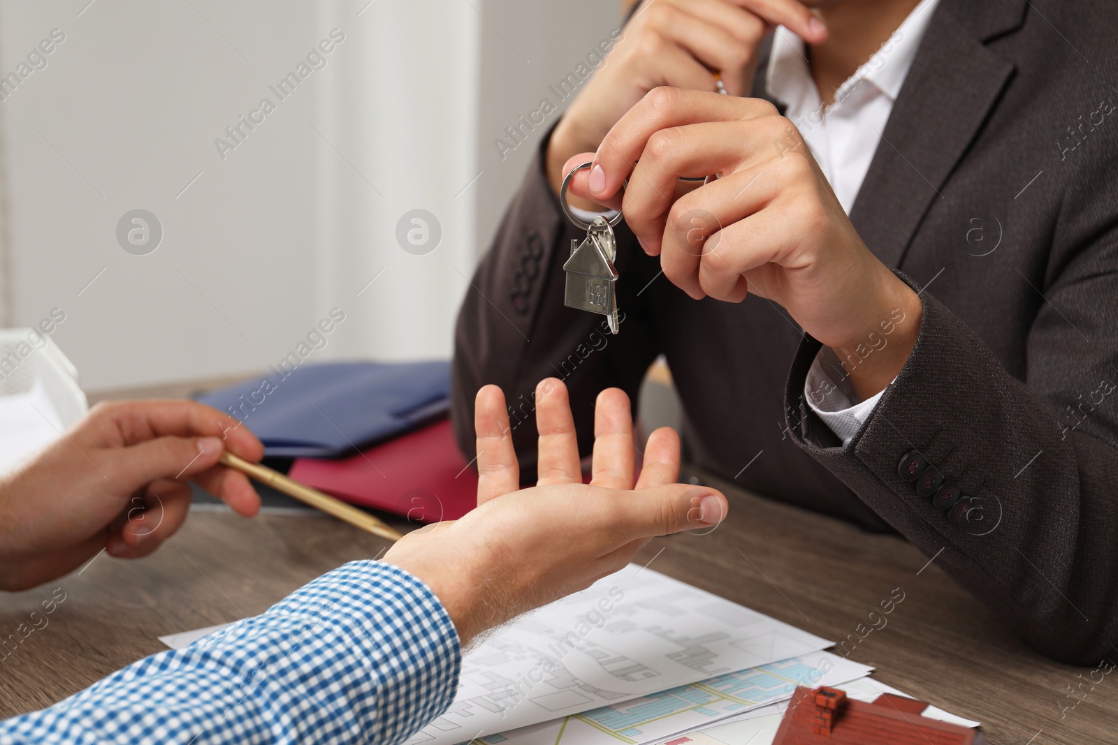 Photo of Real estate agent giving house key to new owner at wooden table, closeup