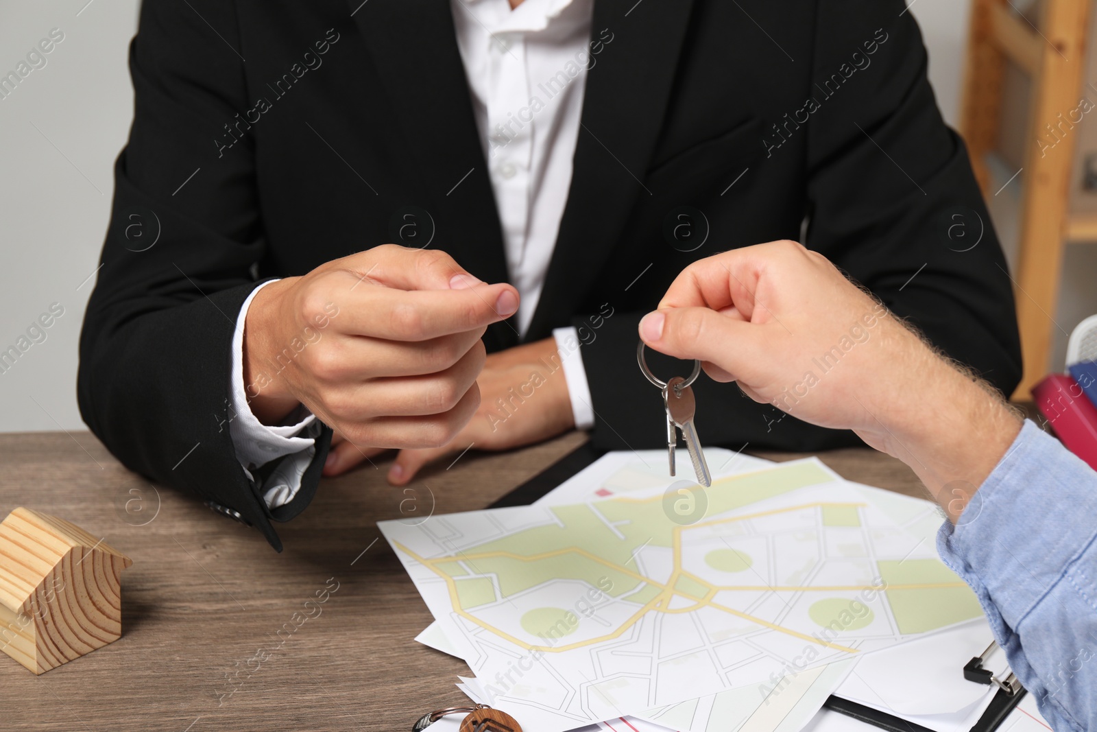 Photo of Real estate agent giving house key to new owner at wooden table, closeup