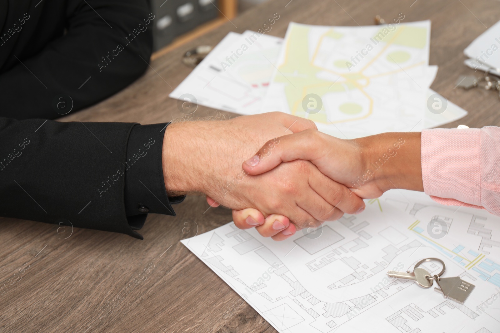 Photo of Real estate agent shaking hands with client at wooden table, closeup