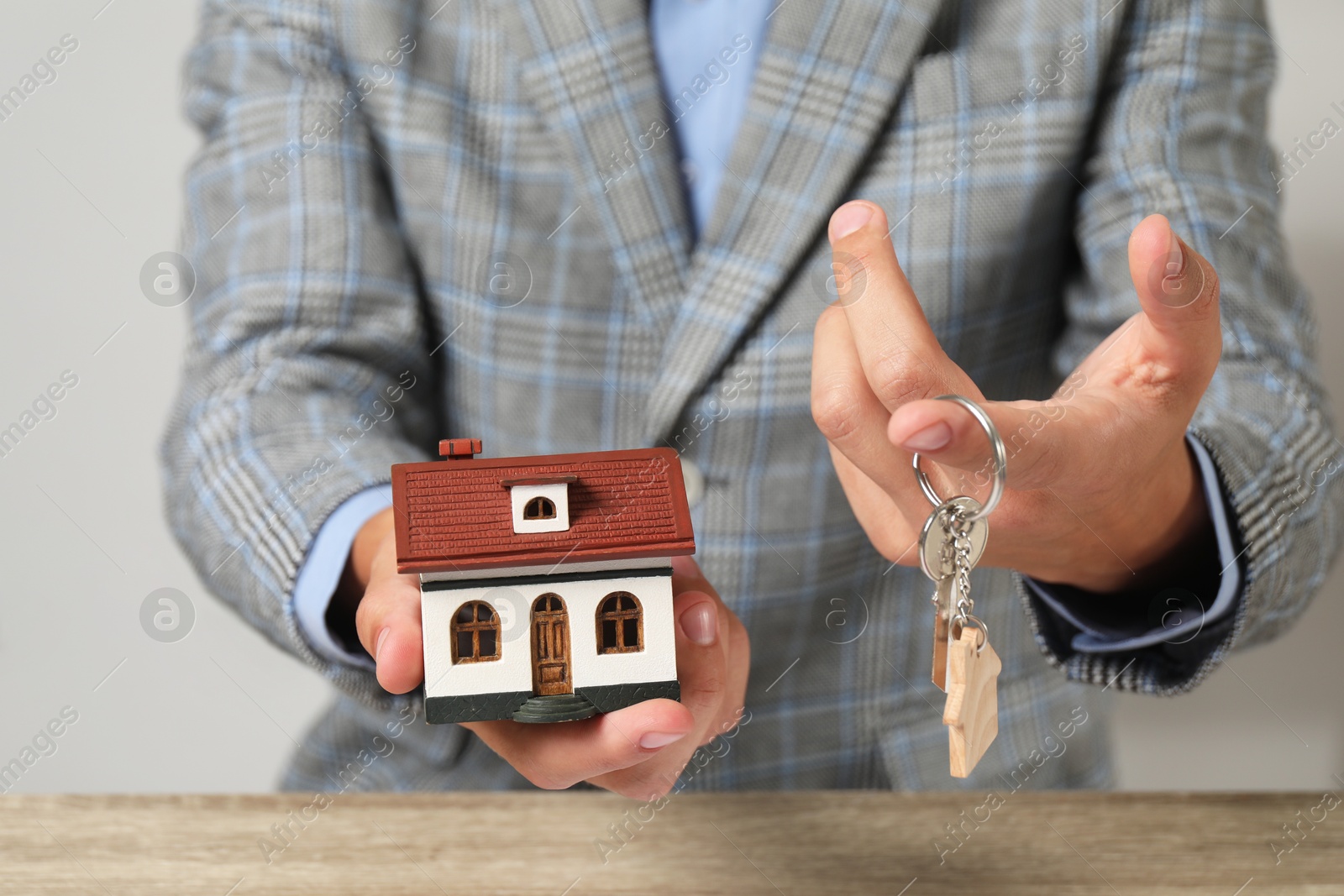 Photo of Real estate agent with key and house model at wooden table, closeup