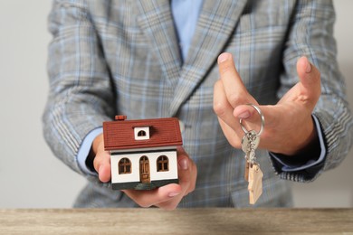 Photo of Real estate agent with key and house model at wooden table, closeup