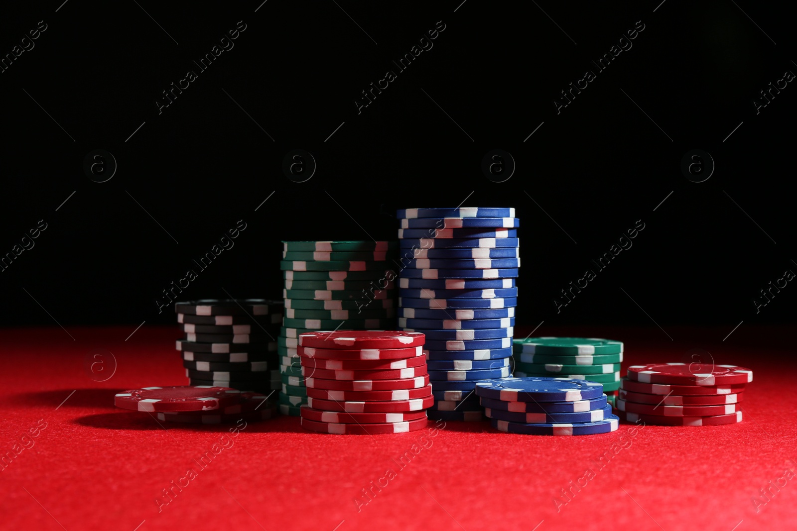 Photo of Poker game. Casino chips on red table against dark background