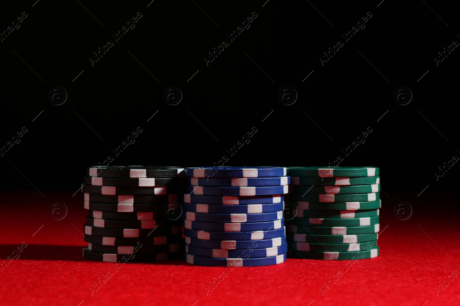 Photo of Poker game. Casino chips on red table against dark background