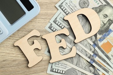 Photo of Word Fed (Federal Reserve System) made with letters, calculator and dollar banknotes on wooden table, flat lay