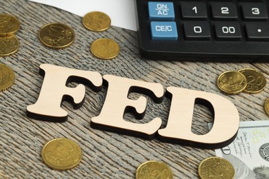 Photo of Word Fed (Federal Reserve System) made with letters, calculator, dollar banknote and coins on wooden table, closeup