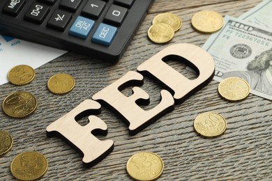 Photo of Word Fed (Federal Reserve System) made with letters, calculator, dollar banknotes and coins on wooden table, closeup