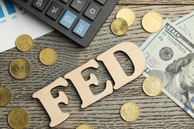 Photo of Word Fed (Federal Reserve System) made with letters, calculator, dollar banknotes and coins on wooden table, flat lay