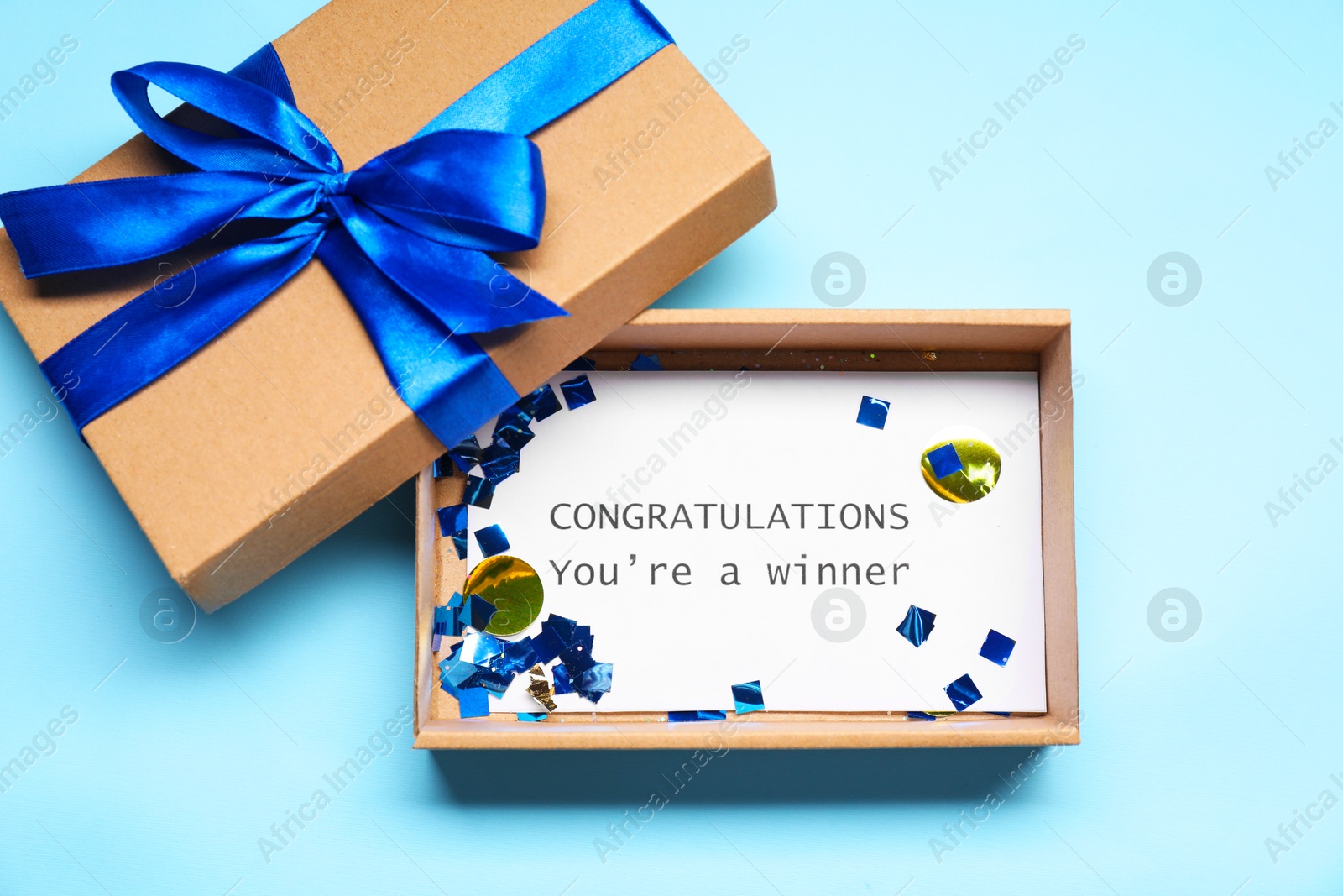 Photo of Card with phrase Congratulations You`re Winner in gift box on light blue background, top view