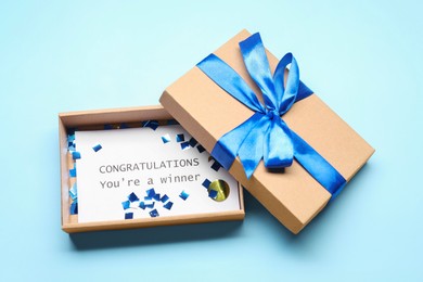 Photo of Card with phrase Congratulations You`re Winner in gift box on light blue background, above view