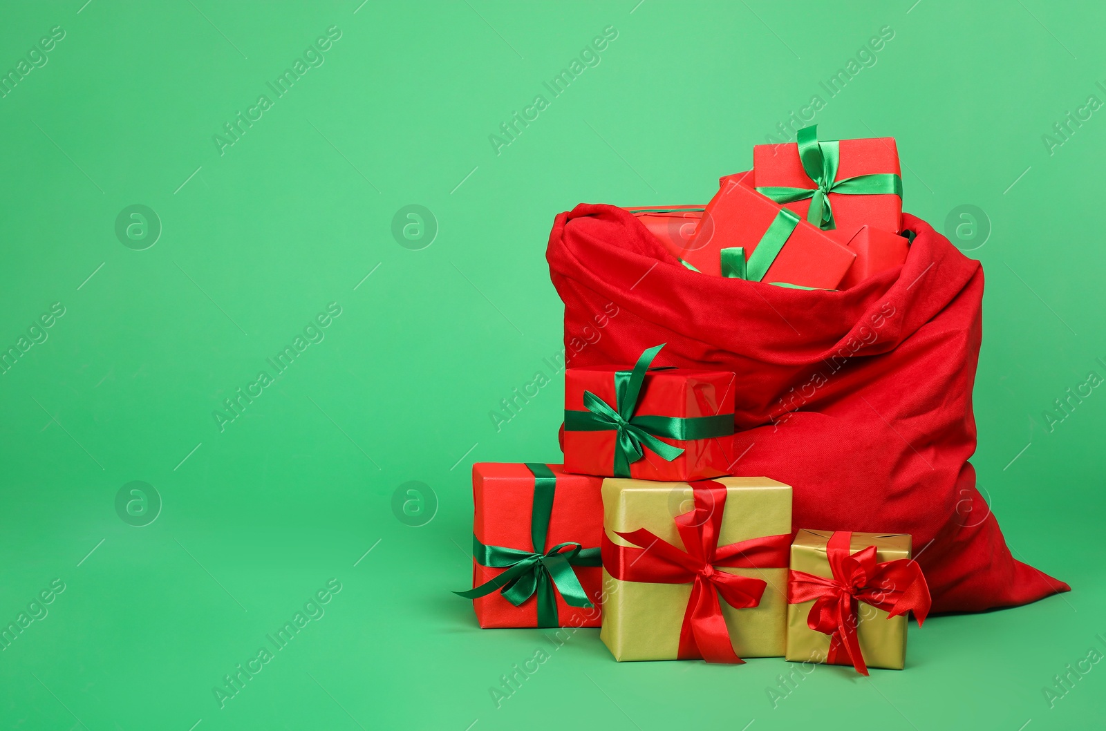 Photo of Red Santa Claus bag with gift boxes on green background, space for text