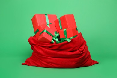 Photo of Red Santa Claus bag with gift boxes on green background