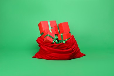 Photo of Red Santa Claus bag with gift boxes on green background