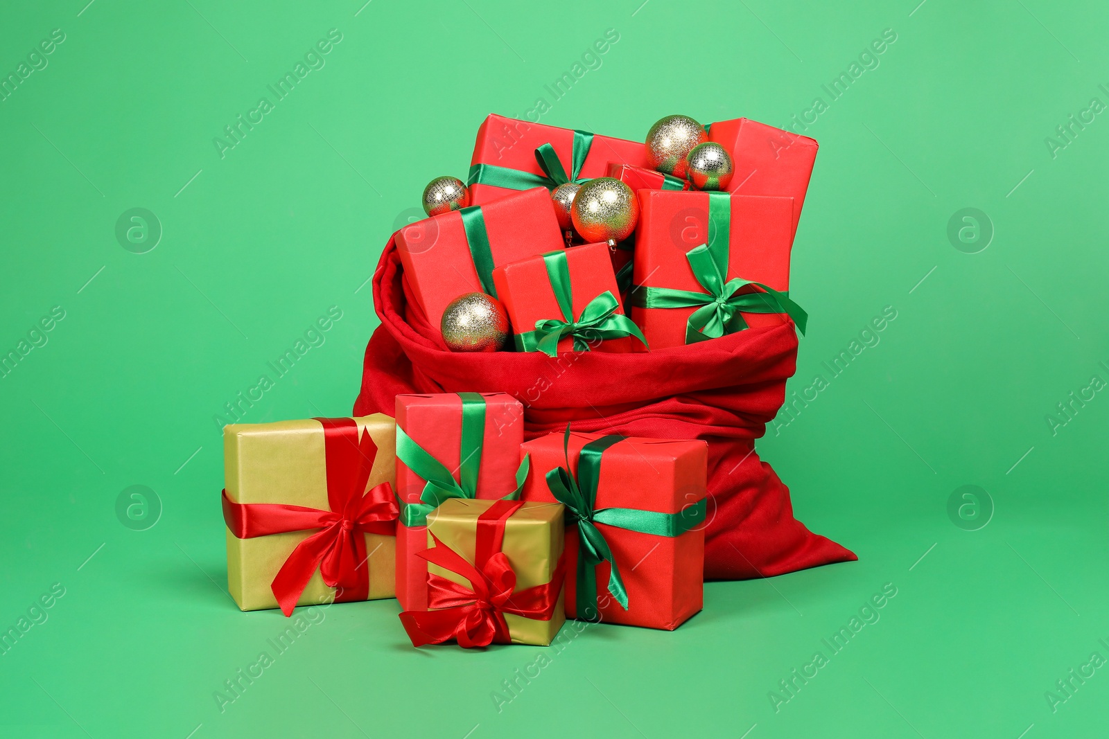 Photo of Red Santa Claus bag with baubles and gift boxes on green background