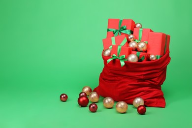 Photo of Red Santa Claus bag with baubles and gift boxes on green background, space for text