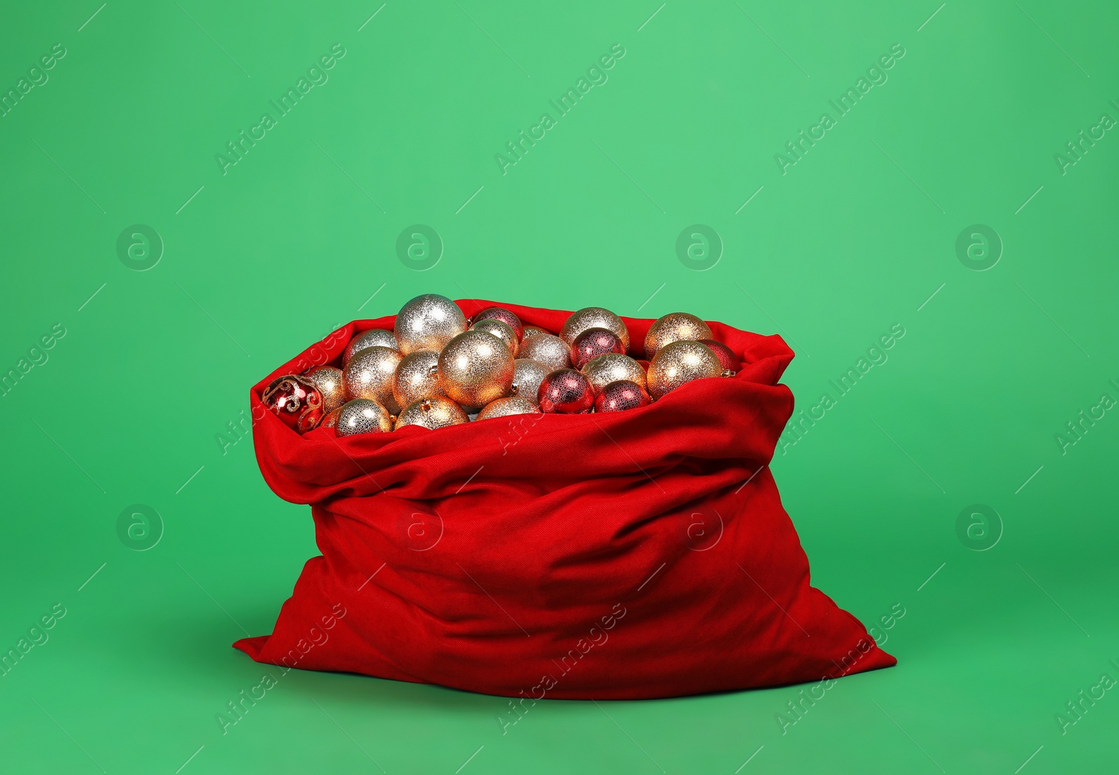 Photo of Red Santa Claus bag with baubles on green background