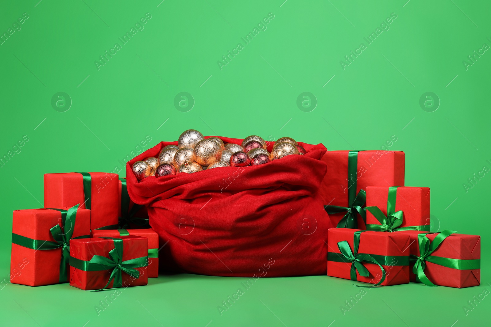 Photo of Red Santa Claus bag with baubles and gift boxes on green background