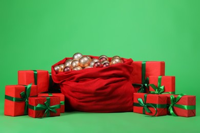 Photo of Red Santa Claus bag with baubles and gift boxes on green background