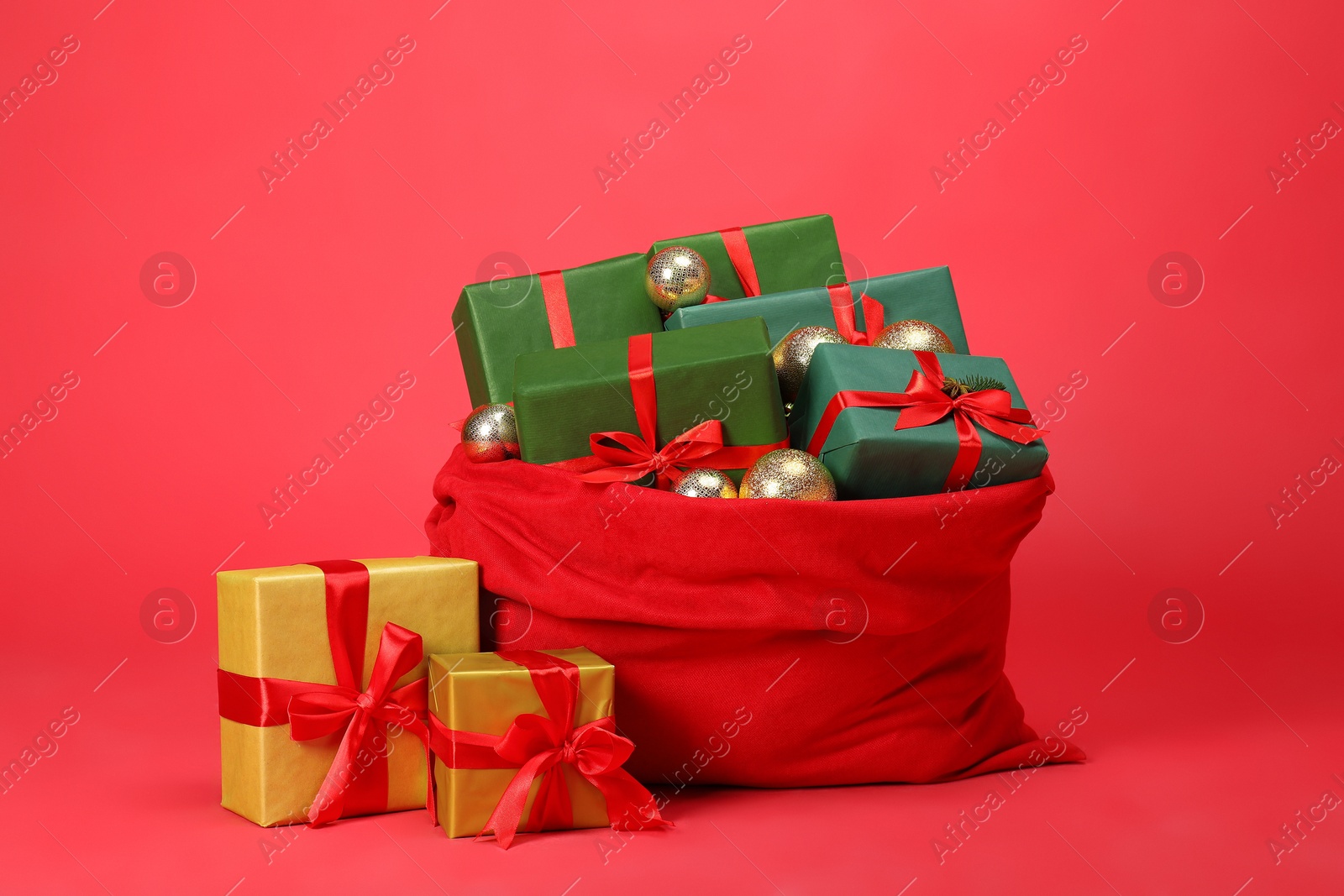 Photo of Santa Claus bag with baubles and gift boxes on red background