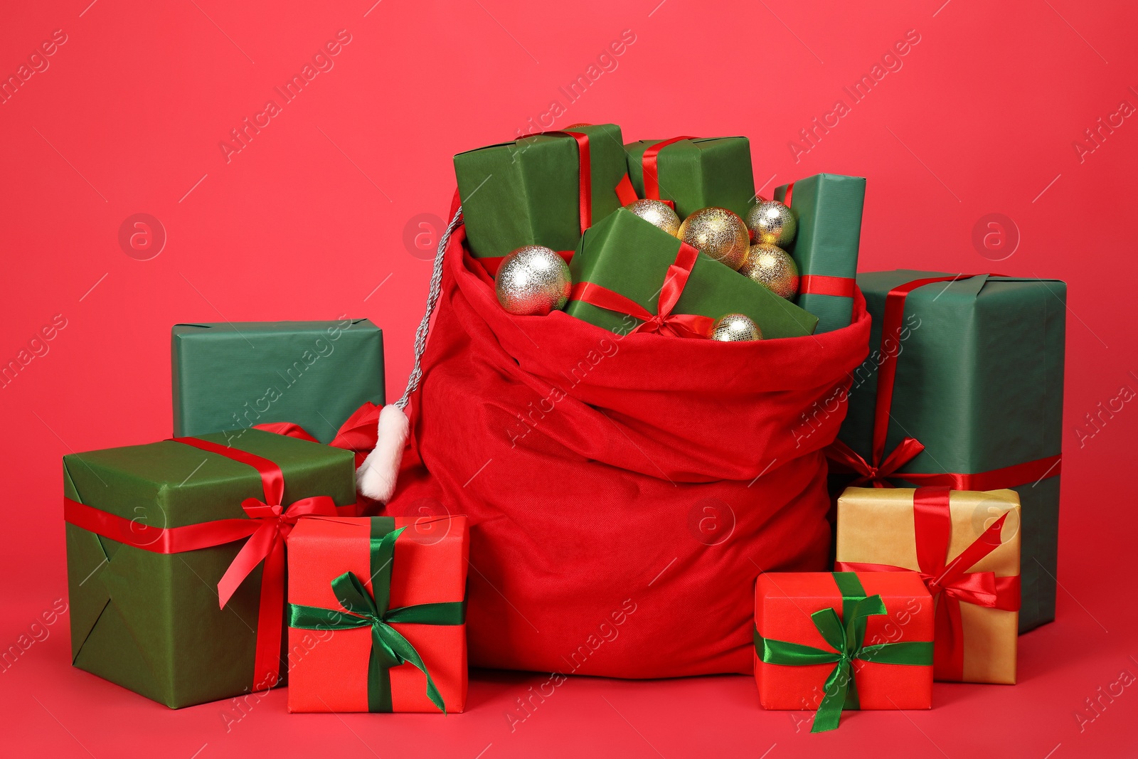 Photo of Santa Claus bag with baubles and gift boxes on red background