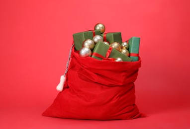 Photo of Santa Claus bag with baubles and gift boxes on red background