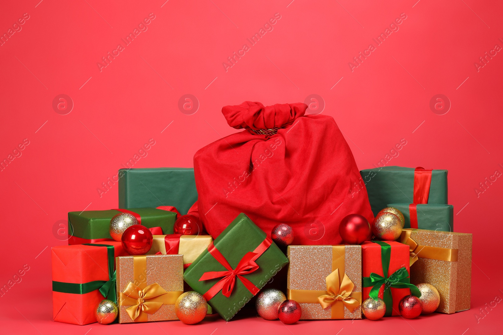 Photo of Santa Claus bag with baubles and gift boxes on red background