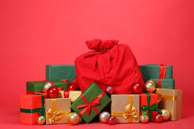 Photo of Santa Claus bag with baubles and gift boxes on red background