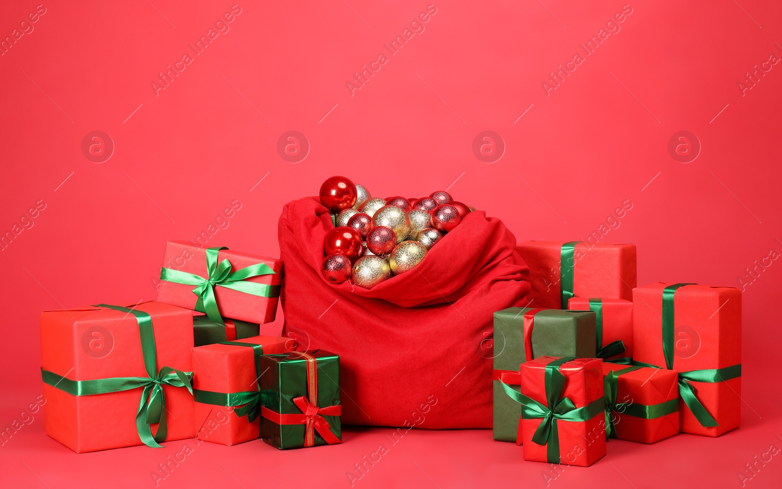 Photo of Santa Claus bag with baubles and gift boxes on red background