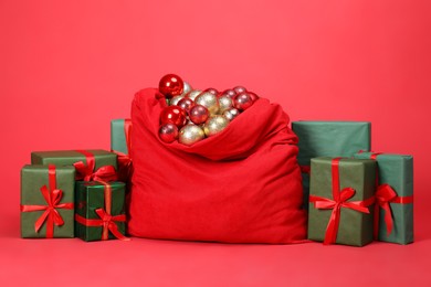 Photo of Santa Claus bag with baubles and gift boxes on red background