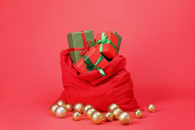 Photo of Santa Claus bag with baubles and gift boxes on red background