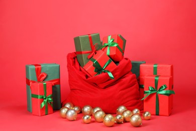 Photo of Santa Claus bag with baubles and gift boxes on red background