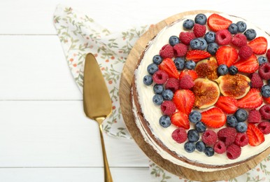 Delicious chocolate sponge cake with berries and server on white wooden table, top view