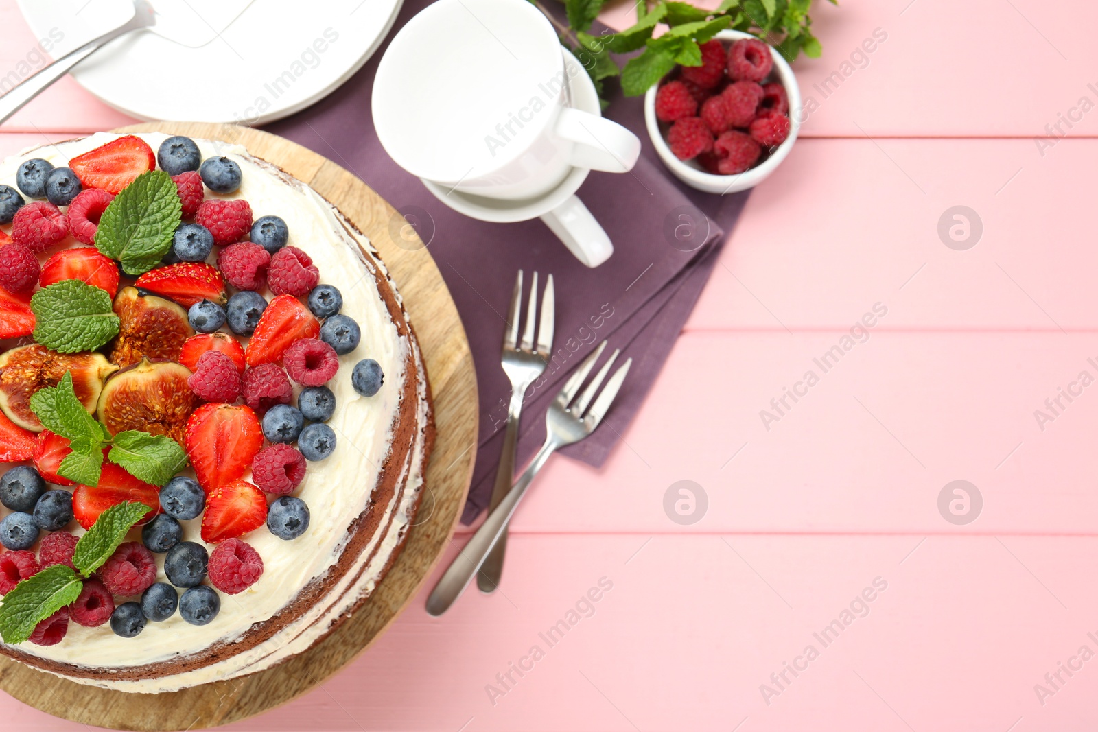 Photo of Delicious chocolate sponge cake with berries served on pink wooden table, top view. Space for text