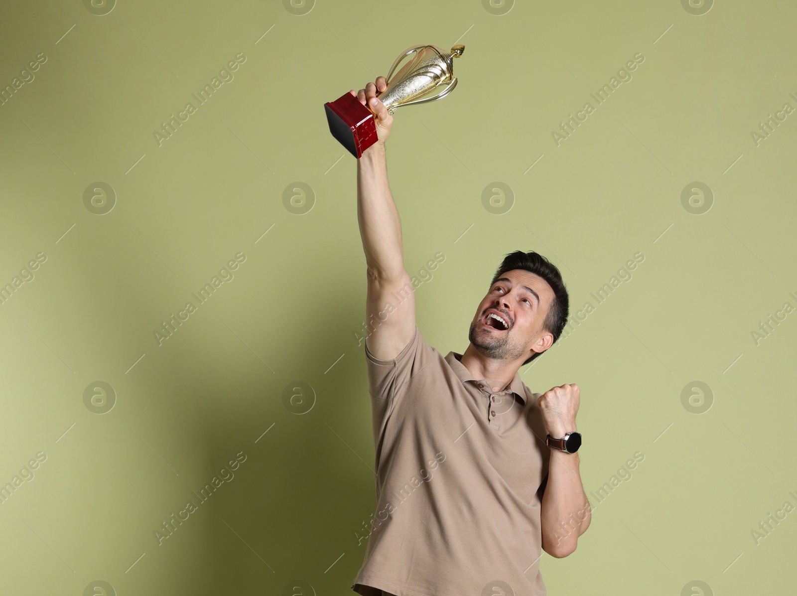 Photo of Happy winner with golden trophy cup on pale olive background, space for text